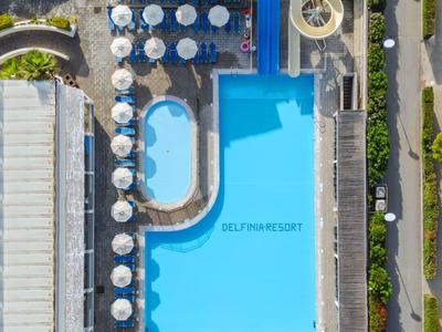 Vista aerea di una piscina d'hotel azzurra con ombrelloni e zona scivolo d'acqua.