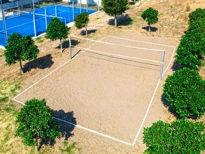 Campo da beach volley vuoto con rete e cespugli verdi intorno, situato in un'area alberghiera.