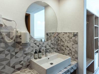 Bagno moderno con piastrelle a motivo geometrico e specchio rotondo.