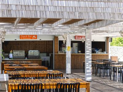 Spazio esterno aperto con tavoli in legno e un bar sotto un tetto bianco.