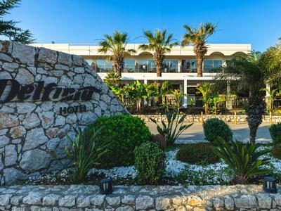 Hotel con edificio bianco circondato da palme e giardino di pietra decorativo sotto un cielo azzurro.