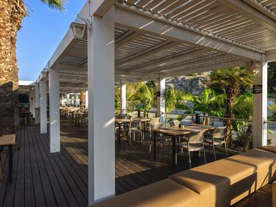 Terrazza esterna coperta con pavimento in legno e posti a sedere in un contesto alberghiero tropicale.