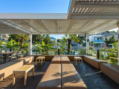 Terrazza esterna coperta con panche imbottite e tavoli, circondata da vegetazione tropicale.
