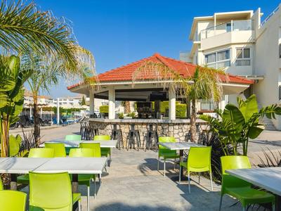 Ristorante all'aperto di un hotel con sedie verdi e palme sotto un cielo sereno.
