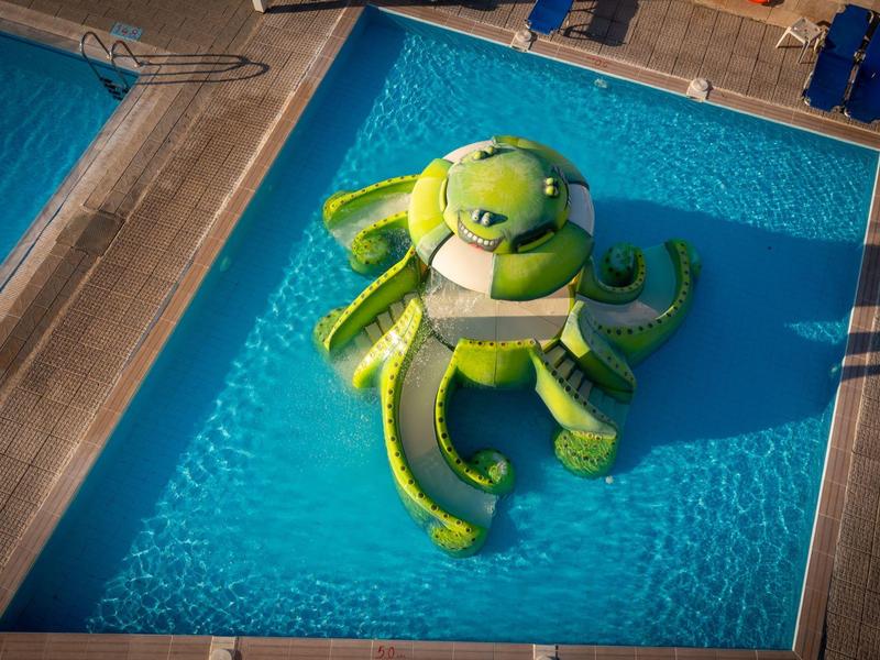 Aufblasbares grünes Oktopus-Spielzeug schwimmt in einem Schwimmbecken neben einer Holzterrasse.