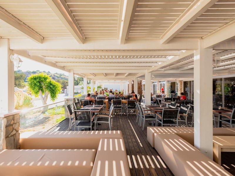 Überdachter Außenbereich eines Restaurants mit Tischen, Stühlen und Sitzbänken bei Tageslicht.