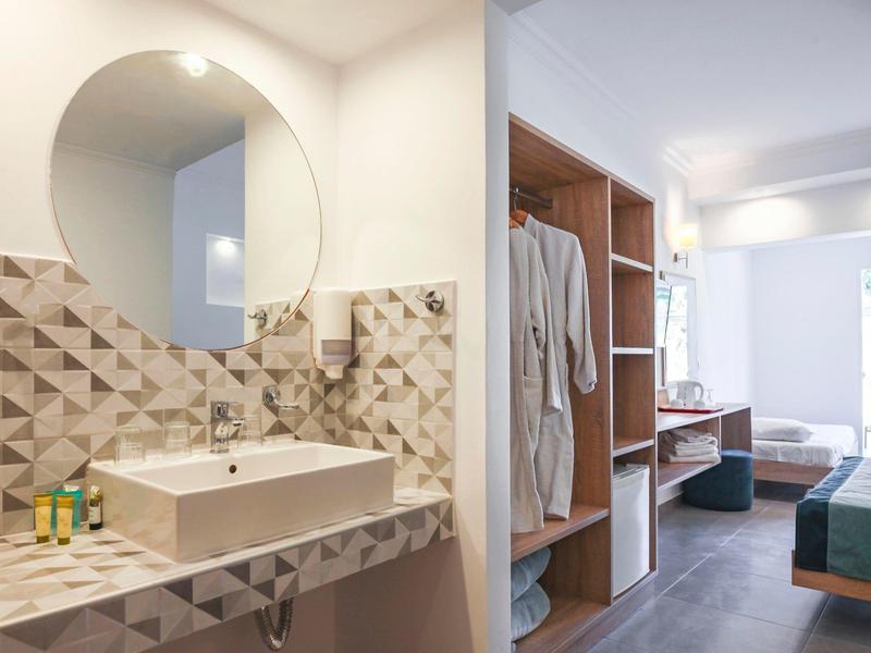 Modernes Hotelzimmer mit Waschbecken, Spiegel und offener Garderobe mit Bademänteln.