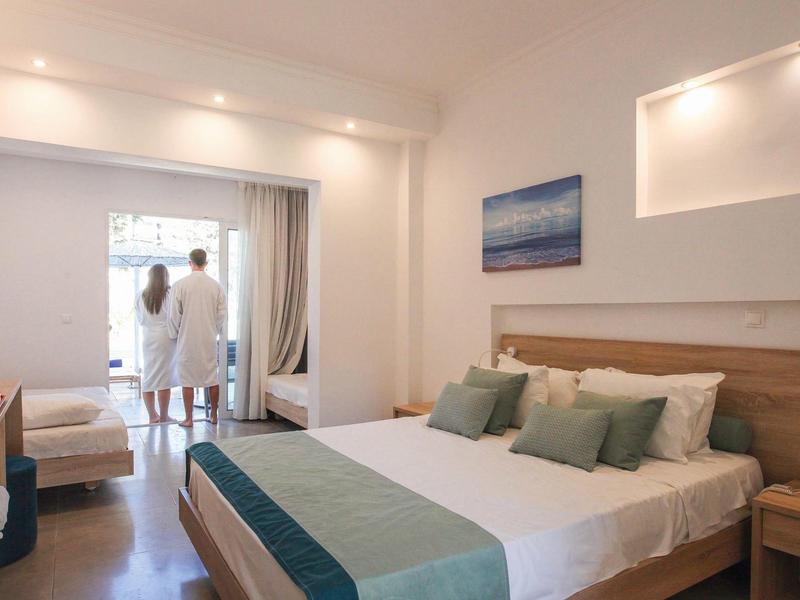 Modernes Hotelzimmer mit Doppelbett, Holzmöbeln und zwei Gästen auf dem Balkon.