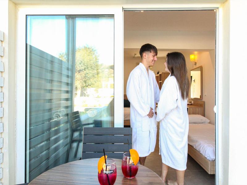 Paar in Bademänteln steht auf Balkon eines Hotelzimmers mit Getränken auf Tisch.