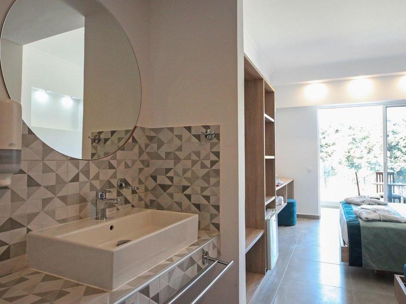 Moderner Hotelbadezimmer mit rundem Spiegel und angrenzendem Wohnbereich mit Terrasse.