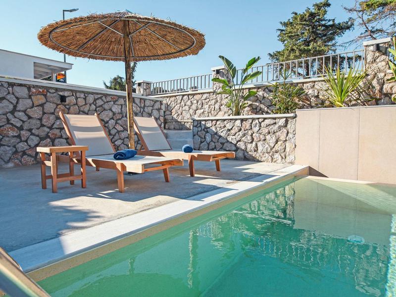 Zwei Liegestühle unter einem Strohs Sonnenschirm neben einem Pool an einem sonnigen Tag.