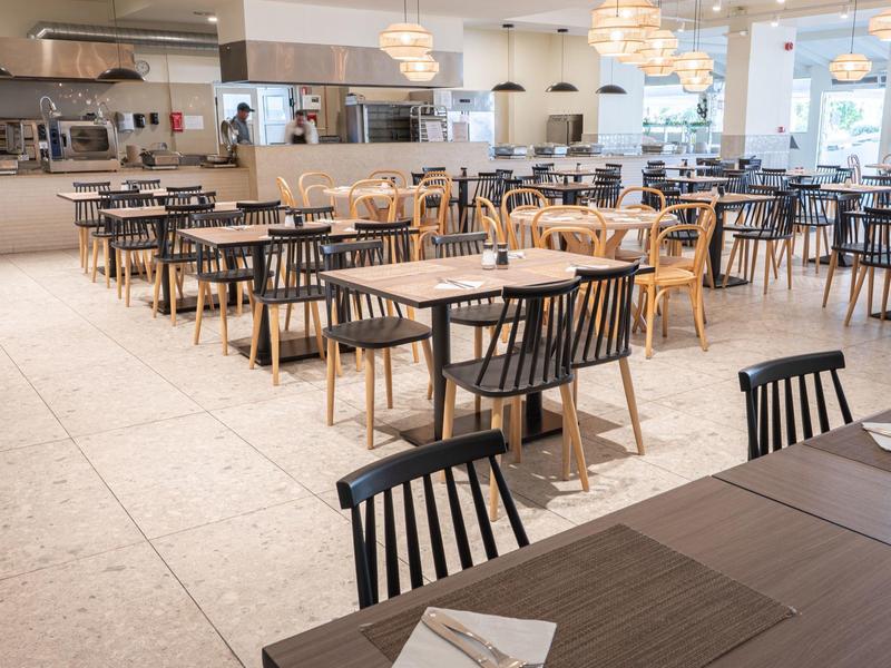 Helles, modernes Restaurant mit Tischen und Stühlen, großen Fenstern und minimalistischem Design.