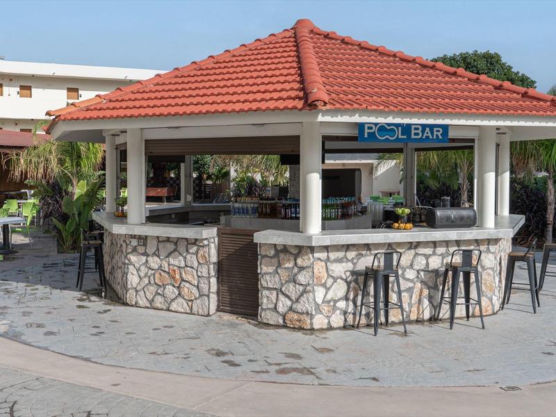 Offene Poolbar mit rotem Ziegeldach und Steinsäulen, umgeben von Barhockern.