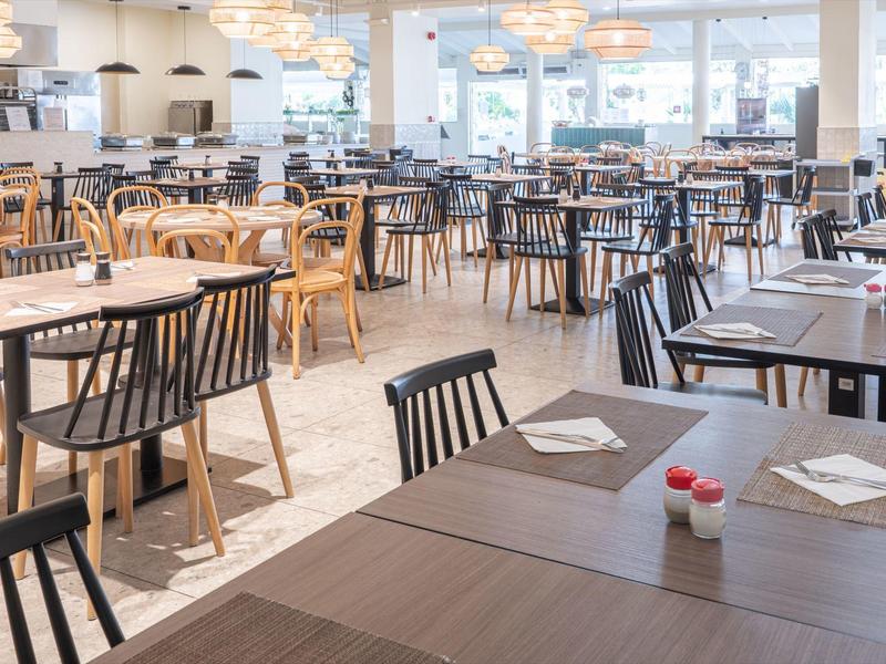 Heller Frühstücksbereich mit verschiedenen Holztischen und Stühlen, moderner und freundlicher Atmosphäre.