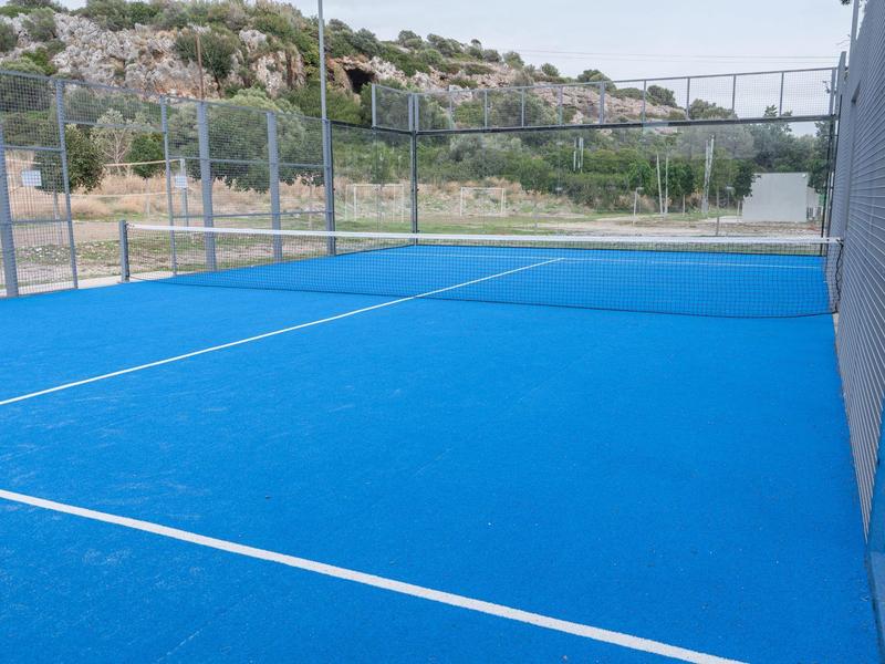 Leerer Tennisplatz mit blauem Belag und umliegendem Zaun in ländlicher Umgebung.