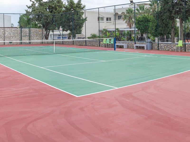 Leerer Tennisplatz mit grünem Spielfeld und rotem Belag im Freien.