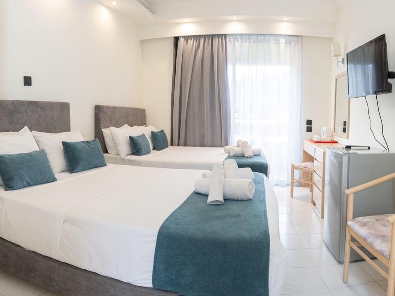 Helles Hotelzimmer mit zwei Einzelbetten, grauen Kopfstützen und blauweißer Bettwäsche.