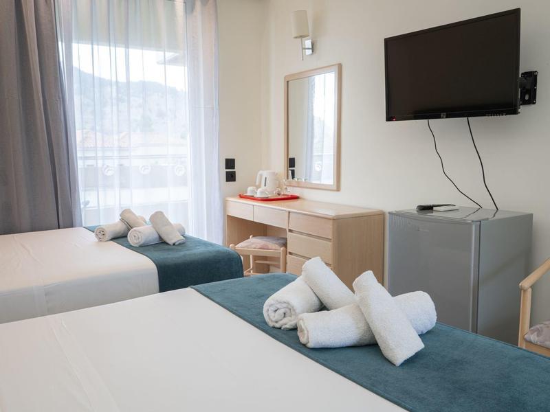 Hell eingerichtetes Hotelzimmer mit zwei Betten, Handtüchern, Fernseher und Schreibtisch.