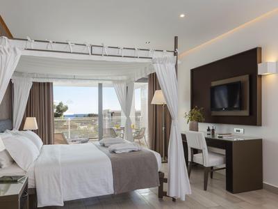 Bright hotel room with canopy bed, desk, and sea view through large windows.