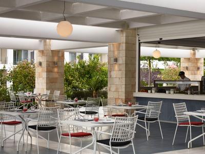 Modern hotel outdoor area with white tables and chairs surrounded by green plants.