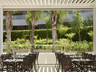 Moderner Außenbereich eines Hotels mit Tischen und Stühlen unter einem überdachten Bereich.