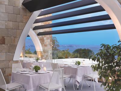 Terrace with set tables overlooking the sea under an arch with wooden beams.