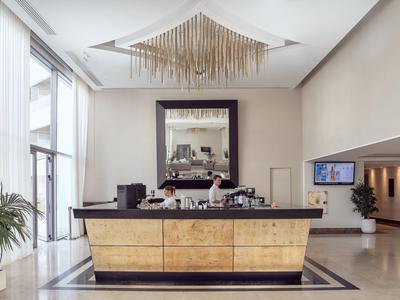 Helle Hotelrezeption mit modernem Empfangstresen, großem Spiegel und floraler Dekoration.