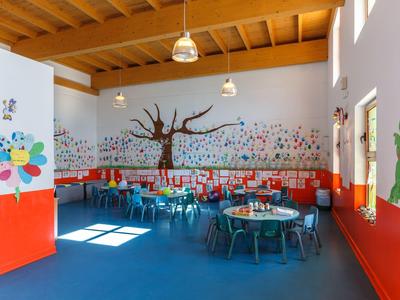 Colorful child-friendly room with tables, chairs, and a painted tree on the wall.