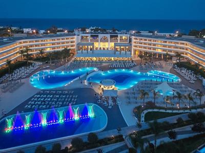 Large hotel with illuminated pools and colorful water fountains at night.