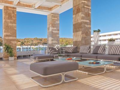 Moderne Lounge im Außenbereich mit gepolsterten Sitzmöbeln, Tischen und Blick auf Pool und Gebäude.