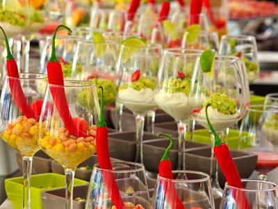 Row of colorful appetizers with chili peppers in elegant wine glasses at a buffet.