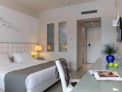 Modern hotel room with large bed, desk, and wall art in neutral tones.
