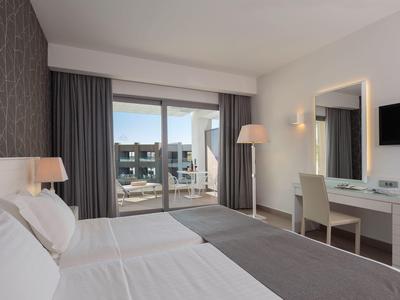 Modern hotel room with double bed, desk, balcony, and view of surrounding buildings.