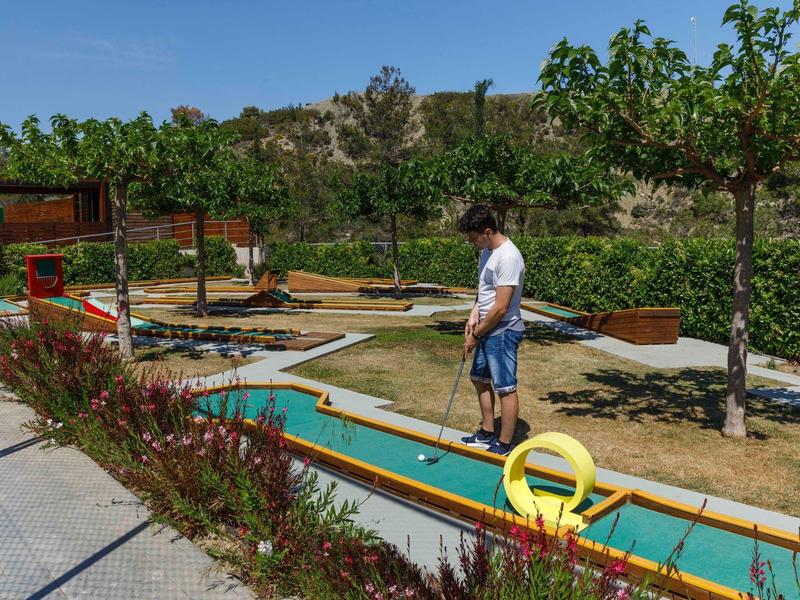 Man playing mini golf on outdoor course with trees and flowers.