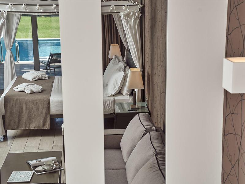 Modern hotel room with bed, sofa, and balcony view overlooking the sea.