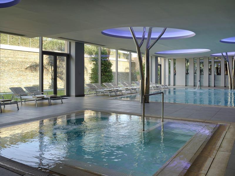 Indoor pool and hot tub with modern seating and large windows.