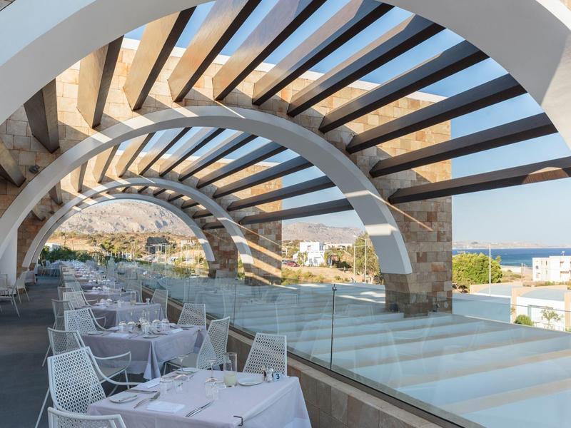 Modern covered terrace with set tables overlooking the sea and buildings.