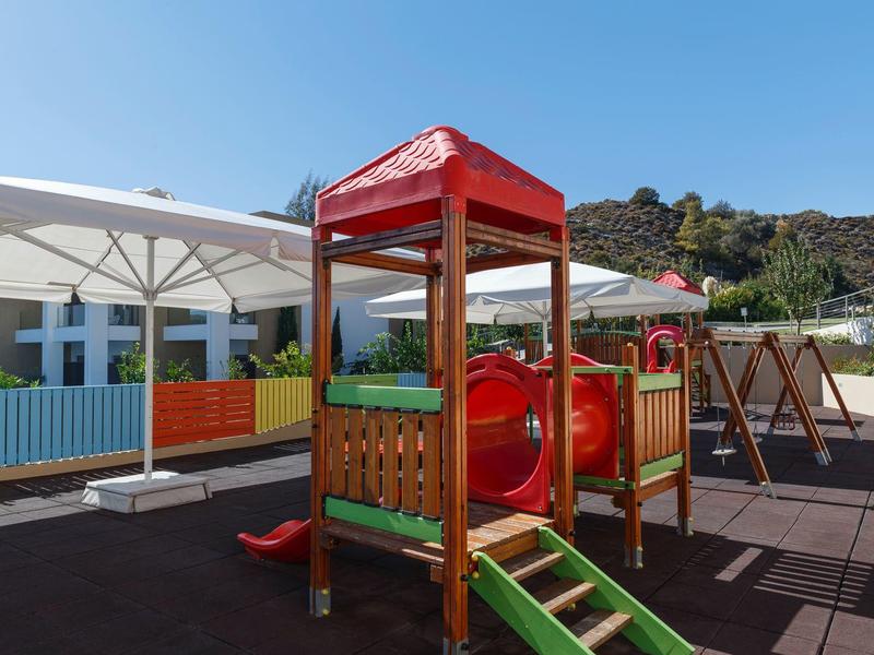 Colorful playground with slide and tunnel on hotel terrace in sunny weather.