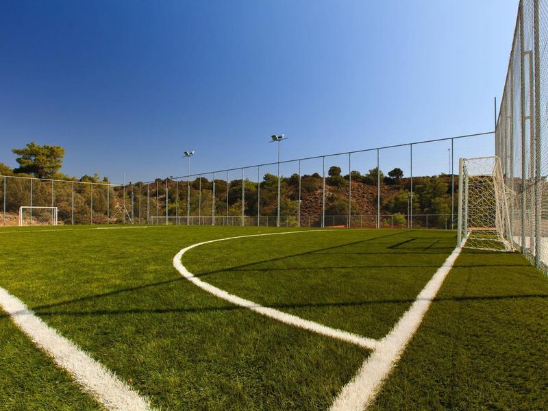 Soccer field with green artificial turf and white lines under a clear blue sky.