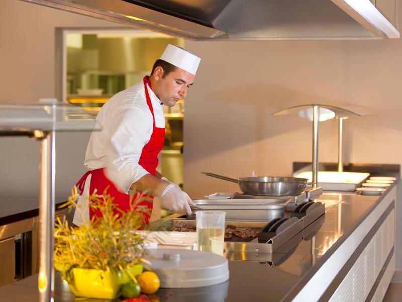 Chef in white hat and red apron cooking in a modern hotel kitchen.