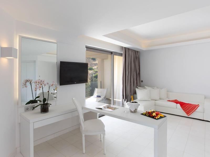 Modern hotel room with white furniture and a terrace overlooking greenery.