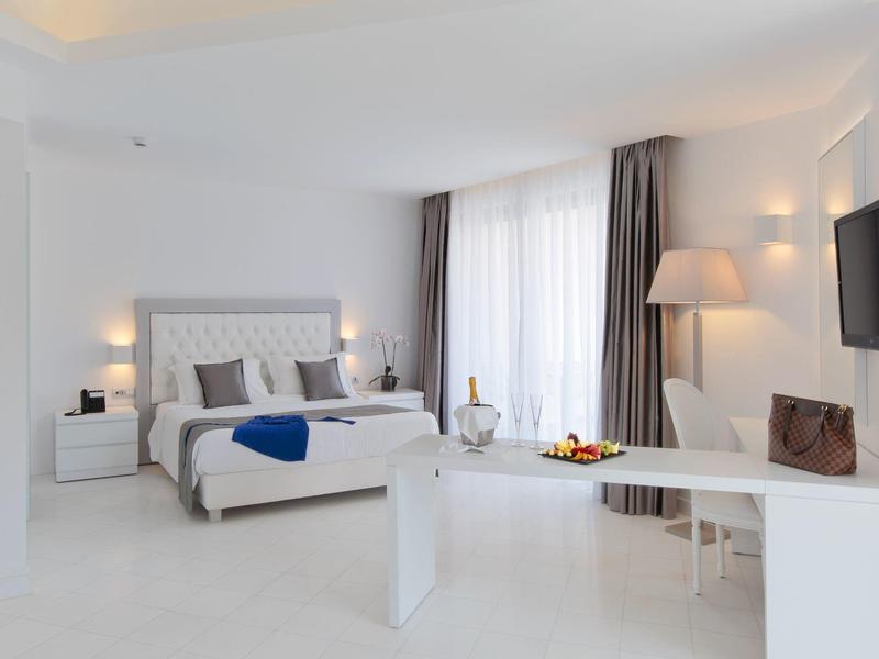 Modern hotel room with large bed, desk, TV, and floor-to-ceiling window with curtains.