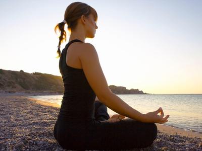 Donna che medita a gambe incrociate sulla spiaggia al tramonto.