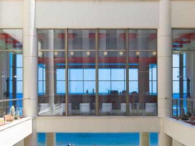 Vista di una terrazza di un hotel moderno con piscina, sedie a sdraio e vista sul mare.