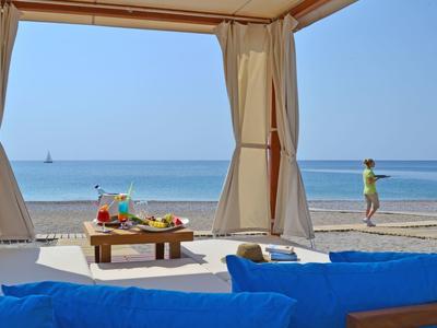 Vista di una spiaggia da una tenda con cuscini blu e tavolino con bevande colorate.