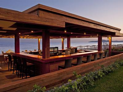 Offene Bar mit Holzdach und Sitzgelegenheiten mit Blick auf das Meer bei Sonnenuntergang.