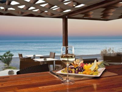Terrasse mit Tisch und Wein unter einem Dach mit Blick auf das Meer bei Sonnenuntergang.
