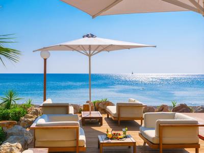 Terrazza sulla spiaggia con sedute e ombrelloni, vista sul mare in una giornata di sole.