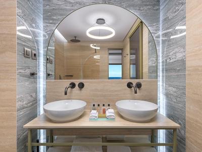 Modernes Badezimmer mit zwei weißen Waschbecken und runden Spiegel, helle Holz- und Marmoroptik.