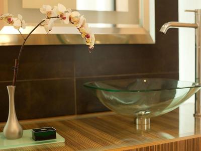 Moderner Hotelwaschtisch mit Glaswaschbecken und blühender Orchidee in Vase.